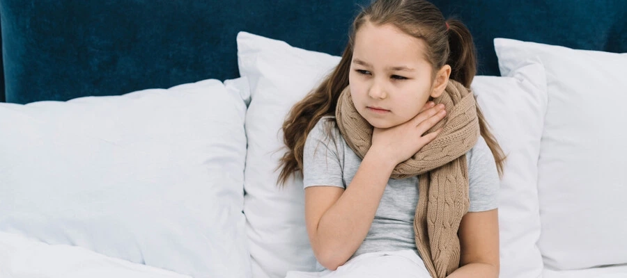 Menina doente sentada na cama com cachecol em volta do pescoço, sofrendo com dor na garganta