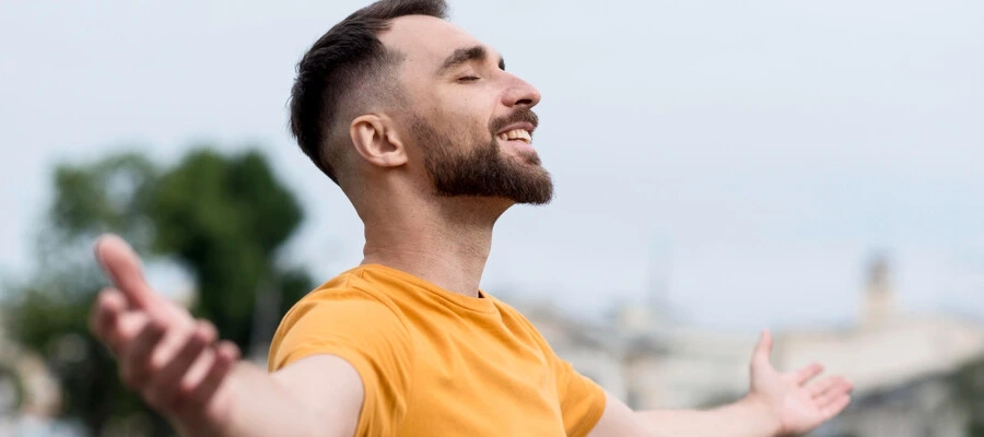 homem com camiseta laranja, feliz ao ar livre com os braços abertos