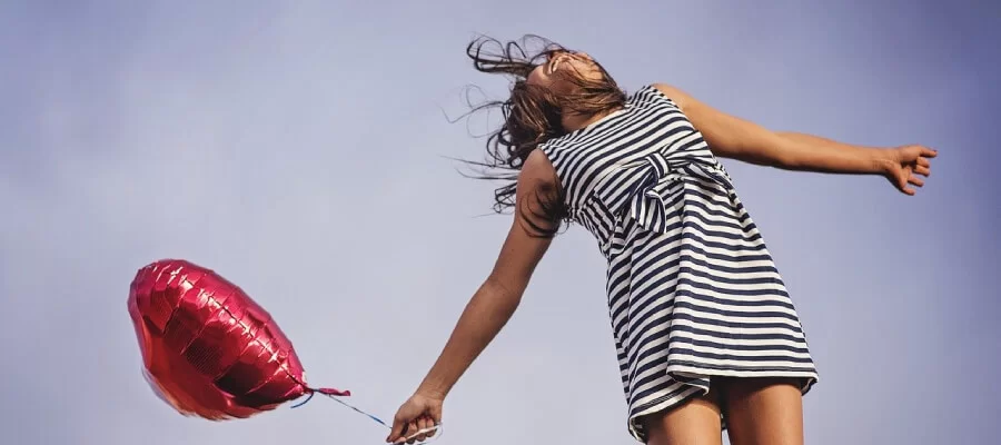 uma menina em um vestido listrado está segurando um balão vermelho