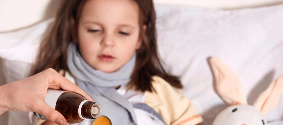 Criança deitada na cama tomando xarope infantil