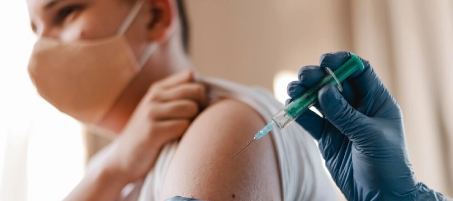 homem com máscara recebendo uma dose de vacina no braço esquerdo. 