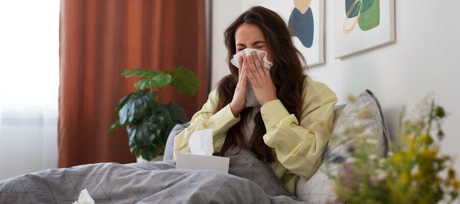 mulher gripada assoando o nariz sentada na cama