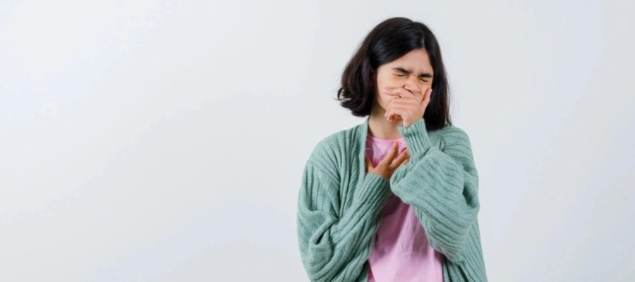Mulher com expressão de dor no peito e tosse, usando casaco verde e camiseta rosa