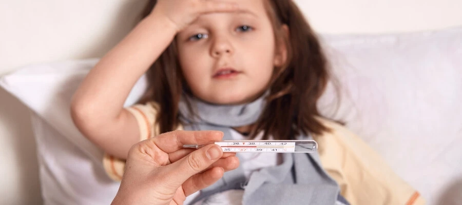 Mão segurando termômetro, menina doente, deitada na cama com a palma da mão na testa