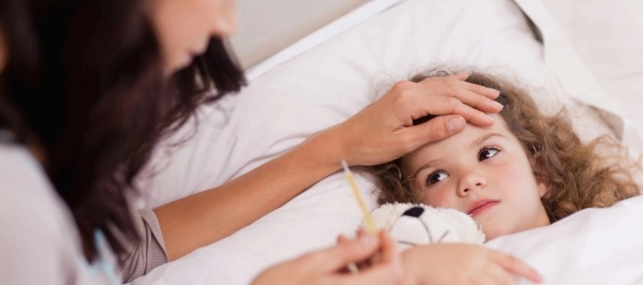 Menina doente deitada na cama enquanto a mãe mede sua temperatura com termômetro.