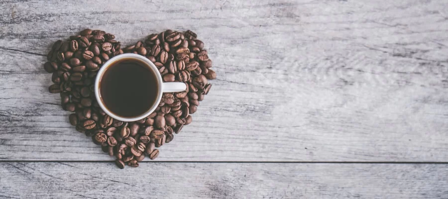 grãos de café em formato de coração com uma xícara no meio