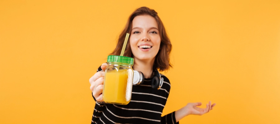 Jovem animada mostrando um copo com suco de laranja e canudo. 
