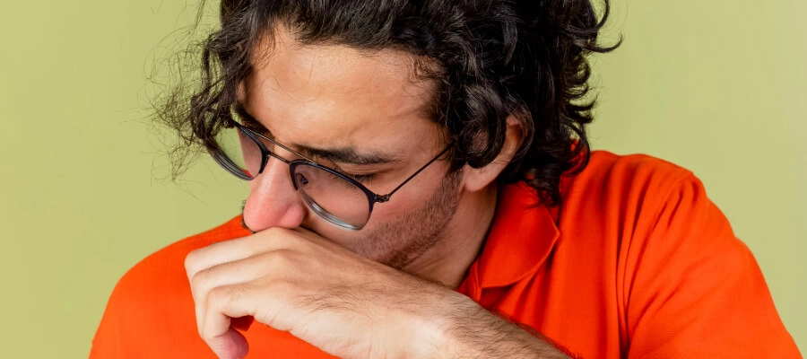 homem de camiseta laranja esfregando o nariz com as mãos