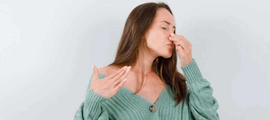 mulher de blusa verde com uma mão no nariz entupido com sensação de falta de ar