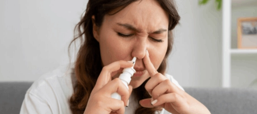 mulher branca tapando uma das narinas enquanto aplica um spray descongestionante no nariz.