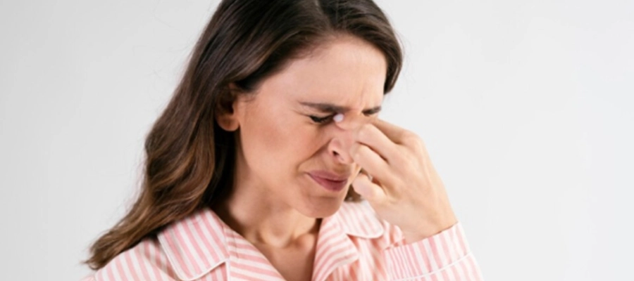 mulher branca de cabelos castanhos, com os olhos fechados e apertando o dorso nasal com expressão de dor