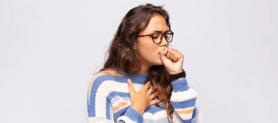 Mulher com óculos e suéter listrado tosse com a mão apoiada no peito.